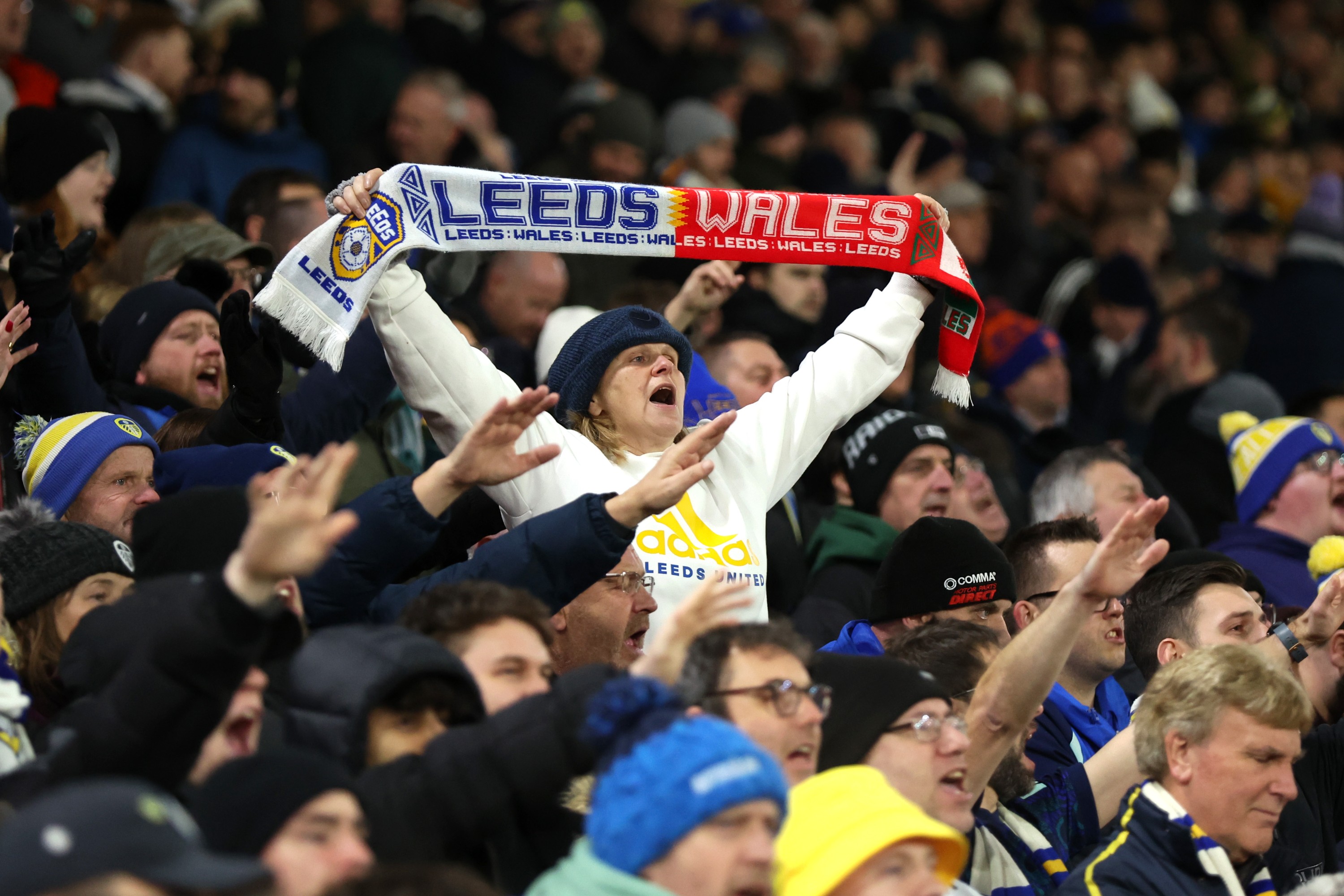 A Leeds United fan raises a Leeds United, Wales scarf